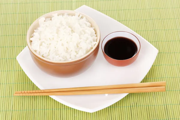 Tigela de arroz e pauzinhos na placa no tapete de bambu — Fotografia de Stock