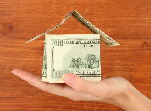 Hand holding a house made of dollars on wooden background close-up — Stock Photo, Image