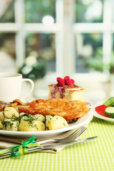 Pečená kuřecí řízek s vařenými brambory a okurky, šálek čaje a zákusek na zelený ubrus v interiér kavárny — Stock fotografie