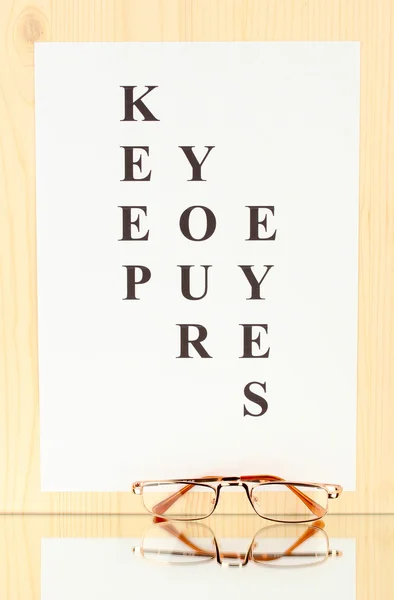 Eyesight test chart with glasses on wooden background close-up — Stock Photo, Image