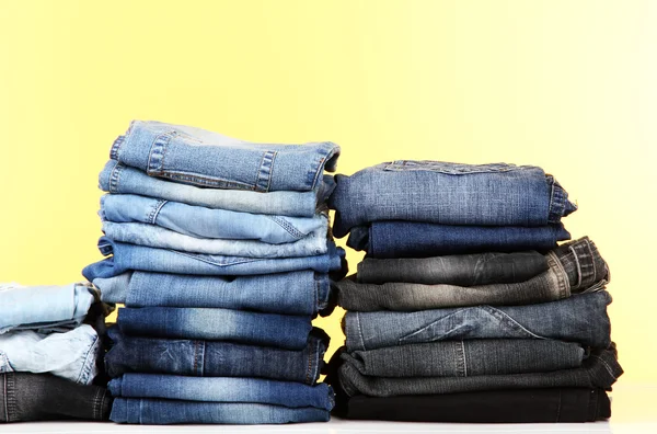 Many jeans stacked in a piles on yellow background — Stock Photo, Image