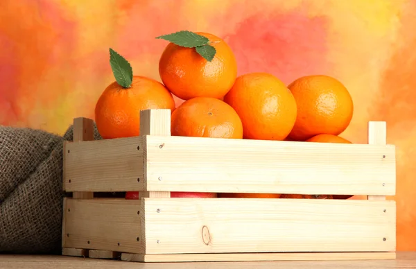 オレンジ色の背景上のテーブルに木製の箱で葉を持つ熟したおいしいみかん — ストック写真