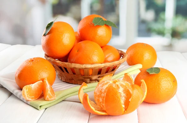 Tangerines with leaves in a beautiful basket, on wooden table on window background — Stock Photo, Image