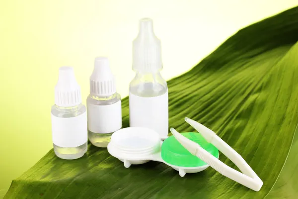 Eye drops and lenses on leaf on green background — Stock Photo, Image