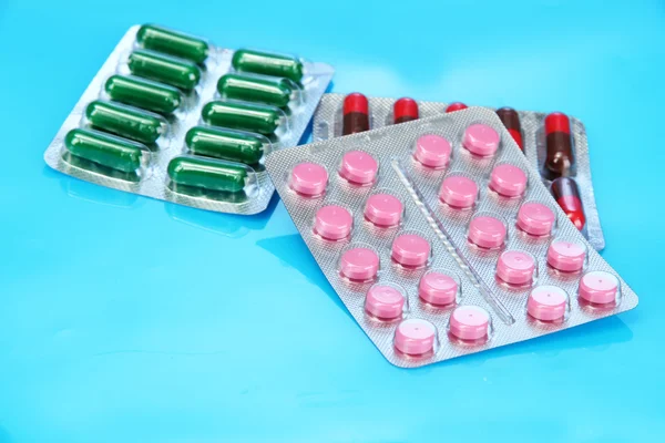 Capsules and pills packed in blisters, on blue background — Stock Photo, Image