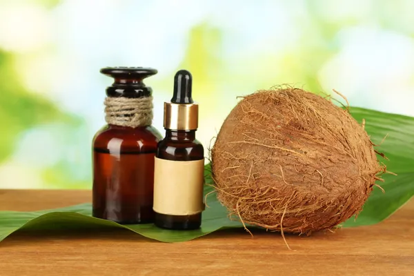 Coconut oil in bottles with coconuts on green background — Stock Photo, Image