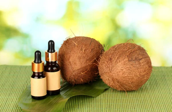 Coconut oil in bottles with coconuts on green background — Stock Photo, Image