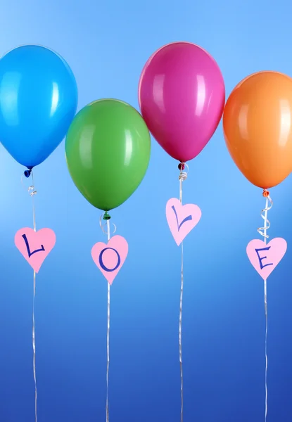 Globos coloridos mantiene la palabra amor sobre fondo azul —  Fotos de Stock