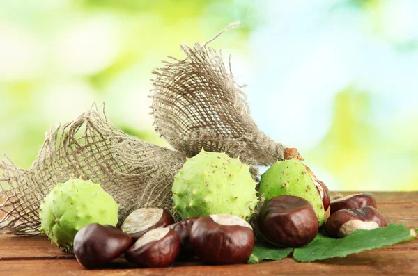 Castanhas com folhas na mesa de madeira em fundo verde — Fotografia de Stock