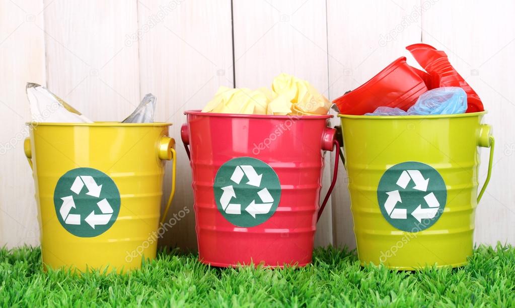 Recycling bins on green grass near wooden fence