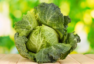 Fresh savoy cabbage on wooden table on natural background