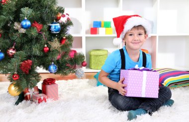 Çocuk Noel Baba şapkası, elinde hediye yılbaşı ağacının yanında oturur