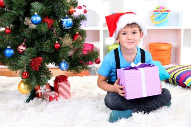 Çocuk Noel Baba şapkası, elinde hediye yılbaşı ağacının yanında oturur
