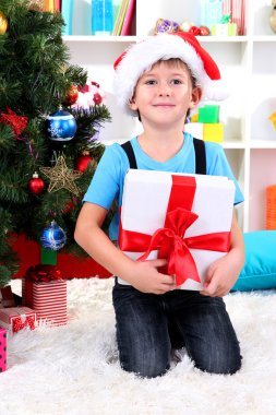 Noel Baba şapkalı küçük çocuk elinde hediye yılbaşı ağacının yanında oturur