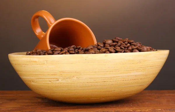 Grains de café dans un bol avec tasse sur la table sur fond brun — Photo