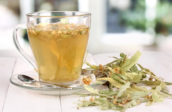 Glass cup of tea with linden on wooden table on window background — Stock Photo, Image