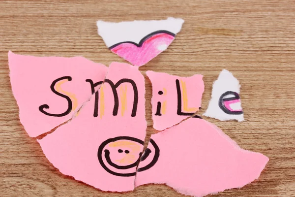 Gescheurd papier met woorden smile close-up op houten tafel — Stockfoto