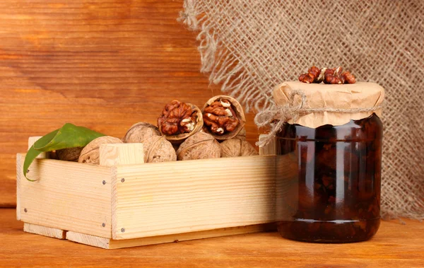 Jam-jar de nozes e caixa de madeira em fundo de madeira — Fotografia de Stock