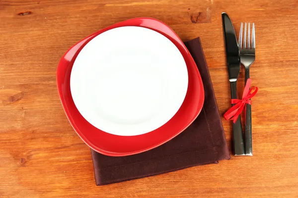 Empty red and white plates with fork and knife on wooden table, close-up — Stock Photo, Image