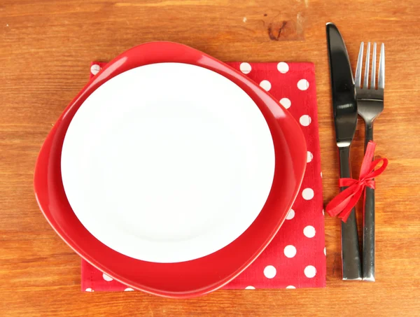 Empty red and white plates with fork and knife on wooden table, close-up — Stock Photo, Image