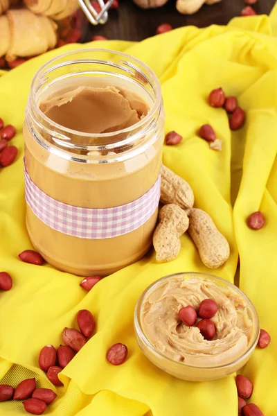 Delicious peanut butter in jar with baking on napkin on wooden table close-up — Stock Photo, Image