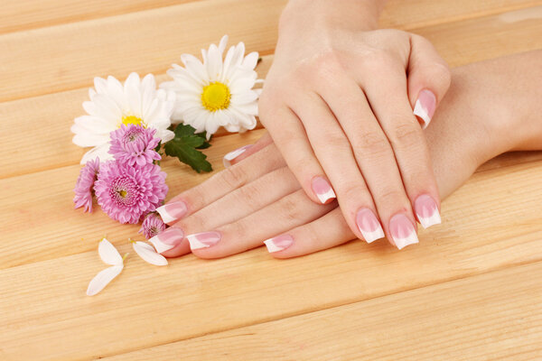 Woman hands with french manicure and flowers on wooden background