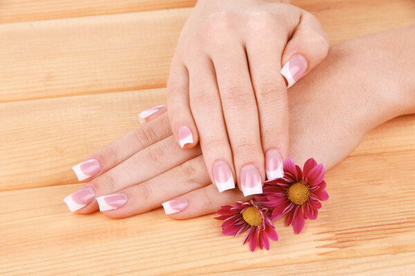 Woman hands with french manicure and flowers on wooden background