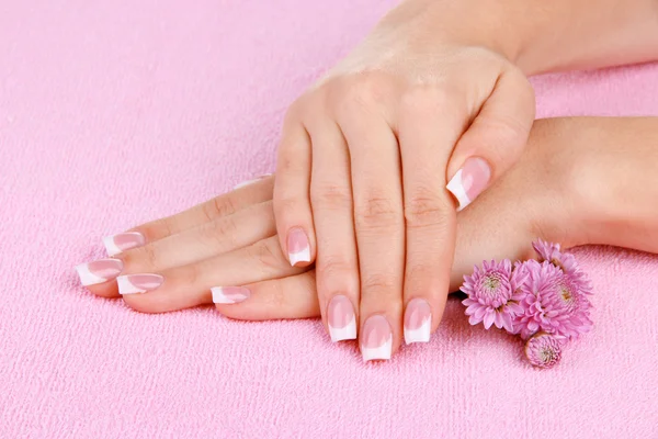 Kobieta ręce z Francuski manicure i kwiaty na różowy ręcznik — Zdjęcie stockowe