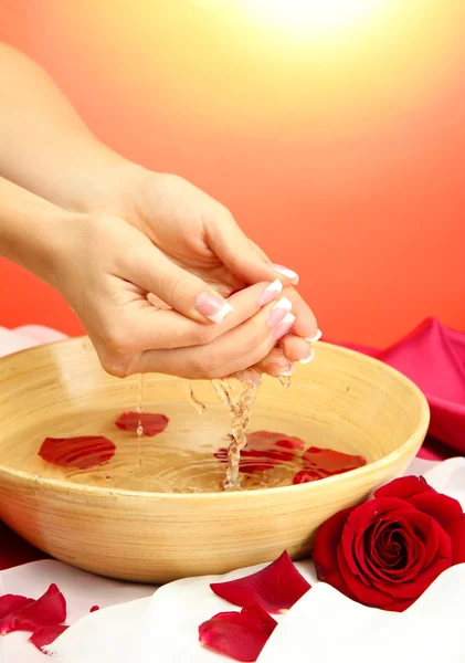 Woman hands with wooden bowl of water with petals, on red background — Stock Photo, Image