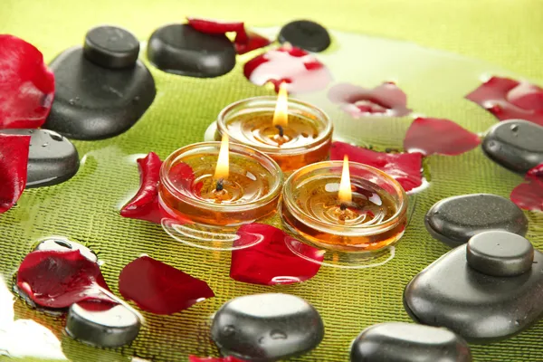 Spa stones with rose petals and candles in water on plate — Stock Photo, Image