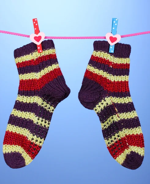 Pair of knit striped socks hanging to dry over blue background — Stock Photo, Image