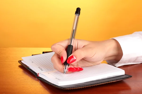 Hand undertecknandet i anteckningsboken på träbord på färgbakgrund — Stockfoto