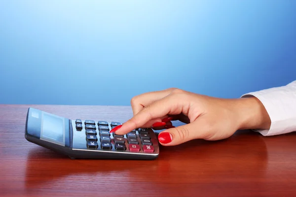 Mains féminines faisant des calculs sur calculatrice sur fond bleu — Photo