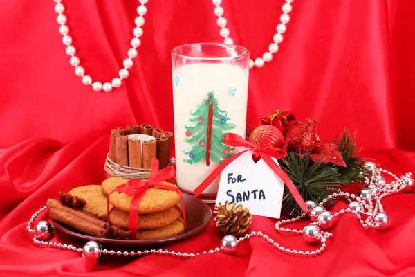 Kekse für den Weihnachtsmann: Konzeptbild von Ingwerplätzchen, Milch und Weihnachtsdekoration auf rotem Hintergrund — Stockfoto