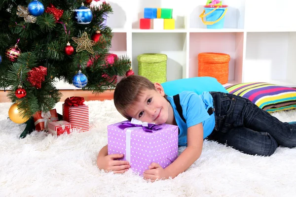 ギフト彼の手に来るサンタ クロースを待っているクリスマス ツリーの下に横たわっている少年 — ストック写真