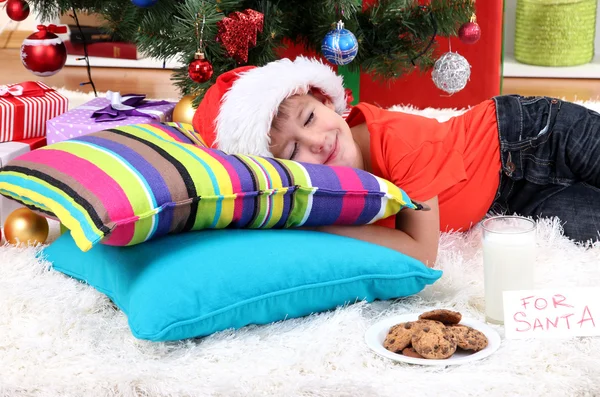 Kleine jongen in Kerstman hoed met melk en koekjes voor santa claus — Stockfoto