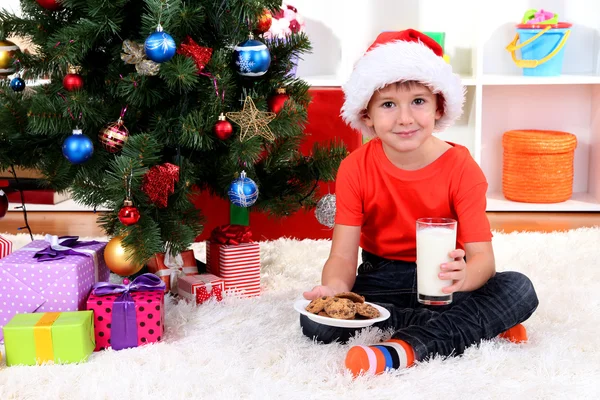 Petit garçon au chapeau de Père Noël avec du lait et des biscuits pour le Père Noël — Photo