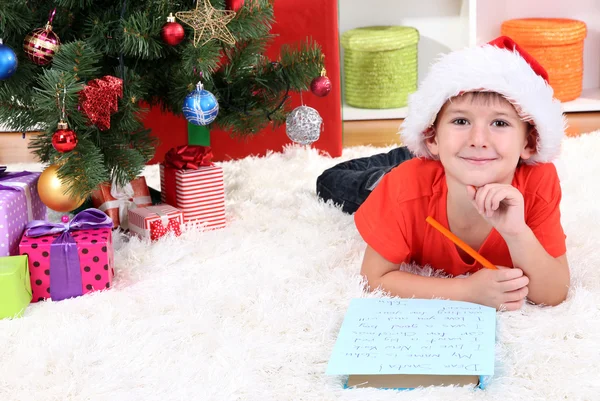 Menino em chapéu de Papai Noel escreve carta para Papai Noel — Fotografia de Stock