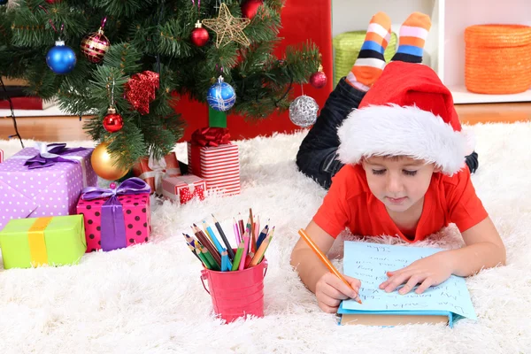 Kleine jongen in Kerstman hoed schrijft een brief aan de Kerstman — Stockfoto