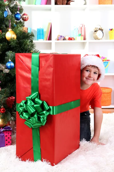 Enfant en chapeau de Père Noël près de l'arbre de Noël avec un grand cadeau — Photo