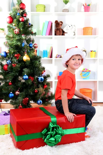 Niño en el sombrero de Santa cerca del árbol de Navidad con gran regalo —  Fotos de Stock