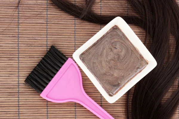 Hair dye in bowl and brush for hair coloring on brown bamboo mat, close-up Stock Picture