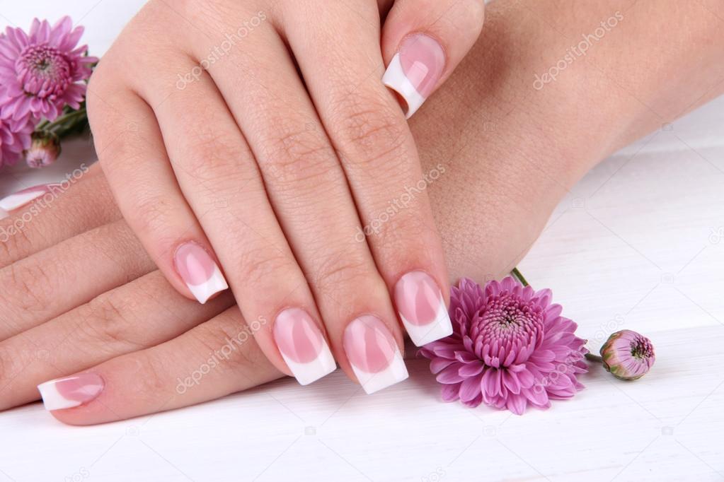 Woman hands with french manicure and flowers on white wooden background