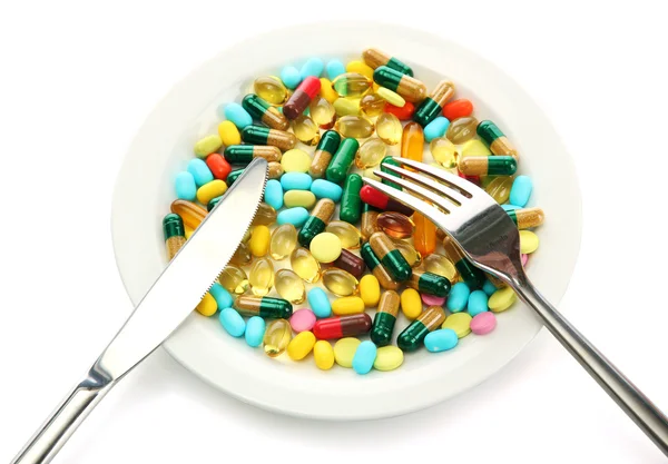 Colorful capsules and pills on plate with fork and knife, isolated on white — Stock Photo, Image