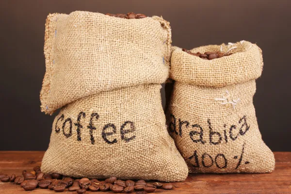 Koffie bonen in zakken op tafel op donkere achtergrond — Stockfoto