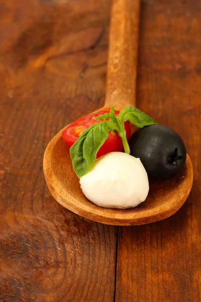 Kaas mozzarella met groenten in houten lepel op houten achtergrond close-up — Stockfoto