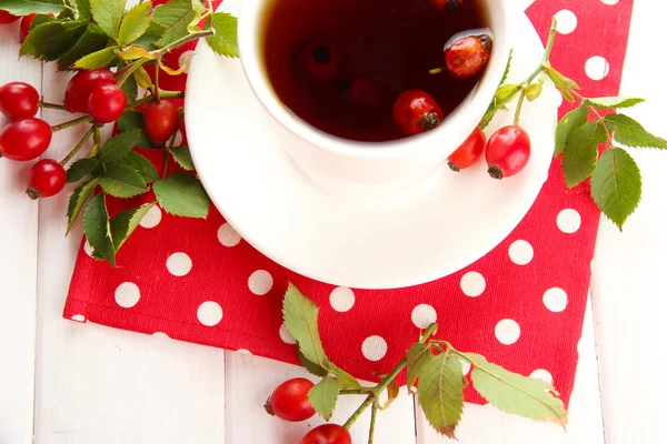 Tasse de thé aux roses de la hanche, sur une table en bois — Photo