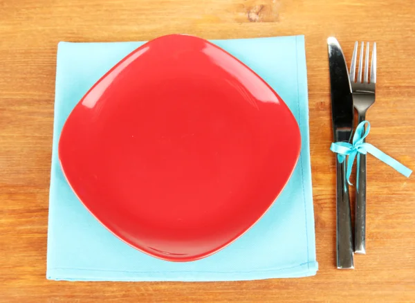 Пустая квадратная красная тарелка с вилкой и ножом на деревянном столе, крупным планом — стоковое фото