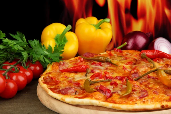 Leckere Pfefferoni-Pizza mit Gemüse auf Holzbrett auf Flammenhintergrund — Stockfoto