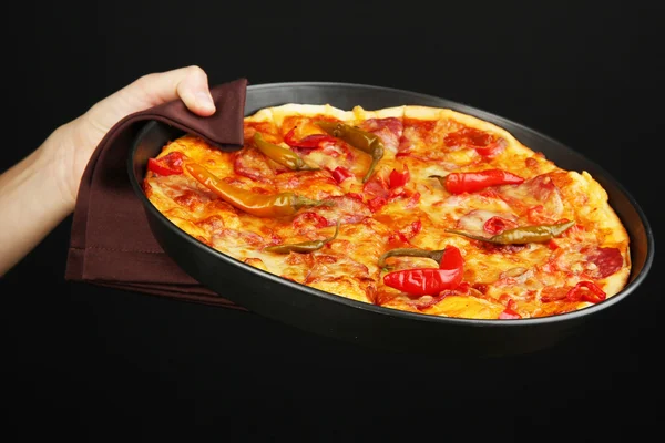 Hand som håller pepperoni pizza i pannan isoleras på svart — Stockfoto